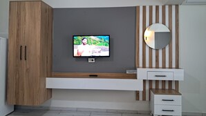 Moderni huone, jossa on harmaaseen seinään asennettu televisio, puiset kaapit, valkoinen konsolipöytä ja peili, jossa on puukuviot.