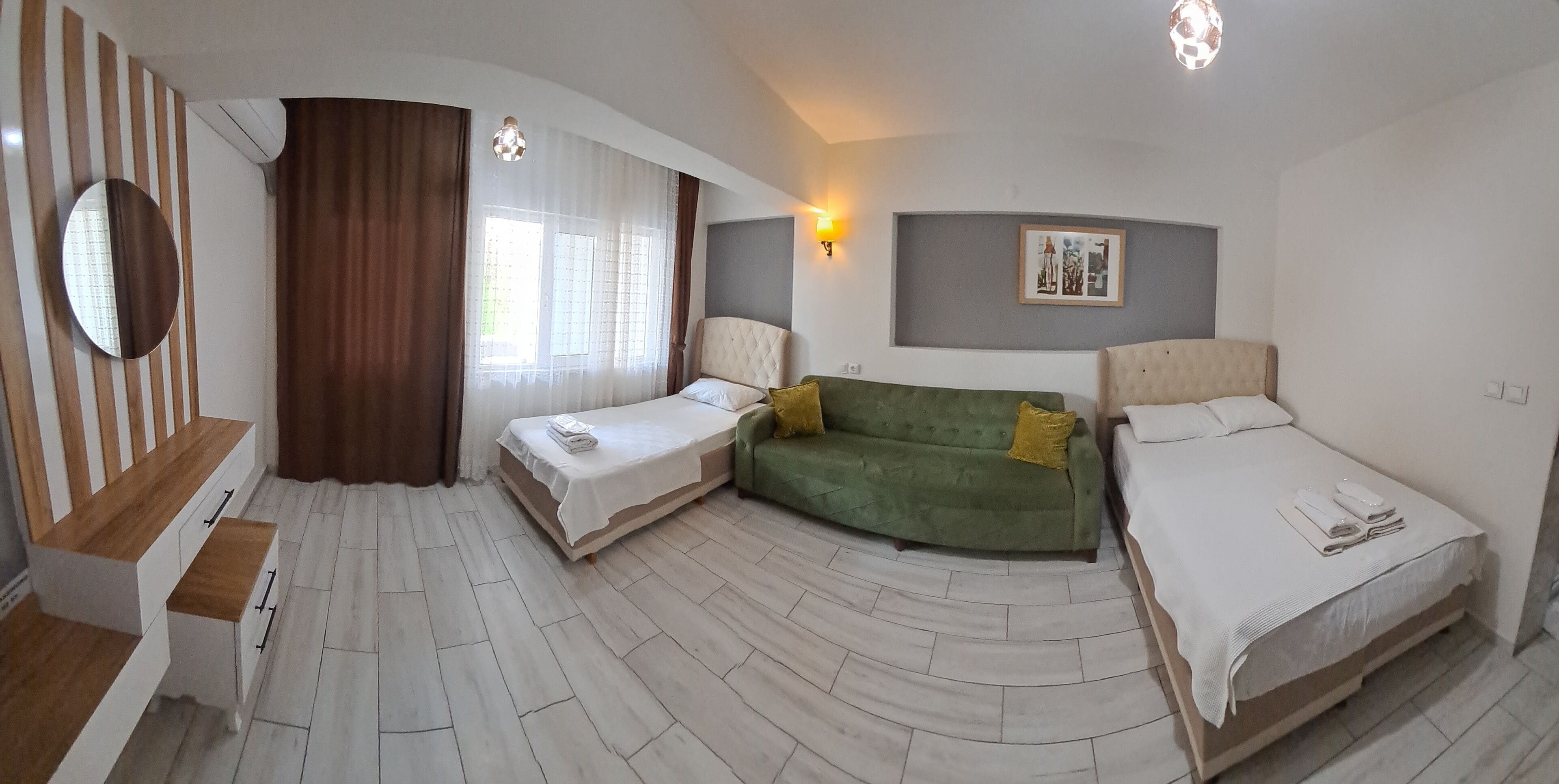 Una habitación de hotel con suelo curvo, un sofá verde, dos camas, un escritorio y un espejo.
