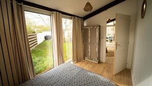 A bedroom with a bed, a window with curtains, a door, and a view of the outside. - Oleron Surf House (Dolus-d'Oléron)