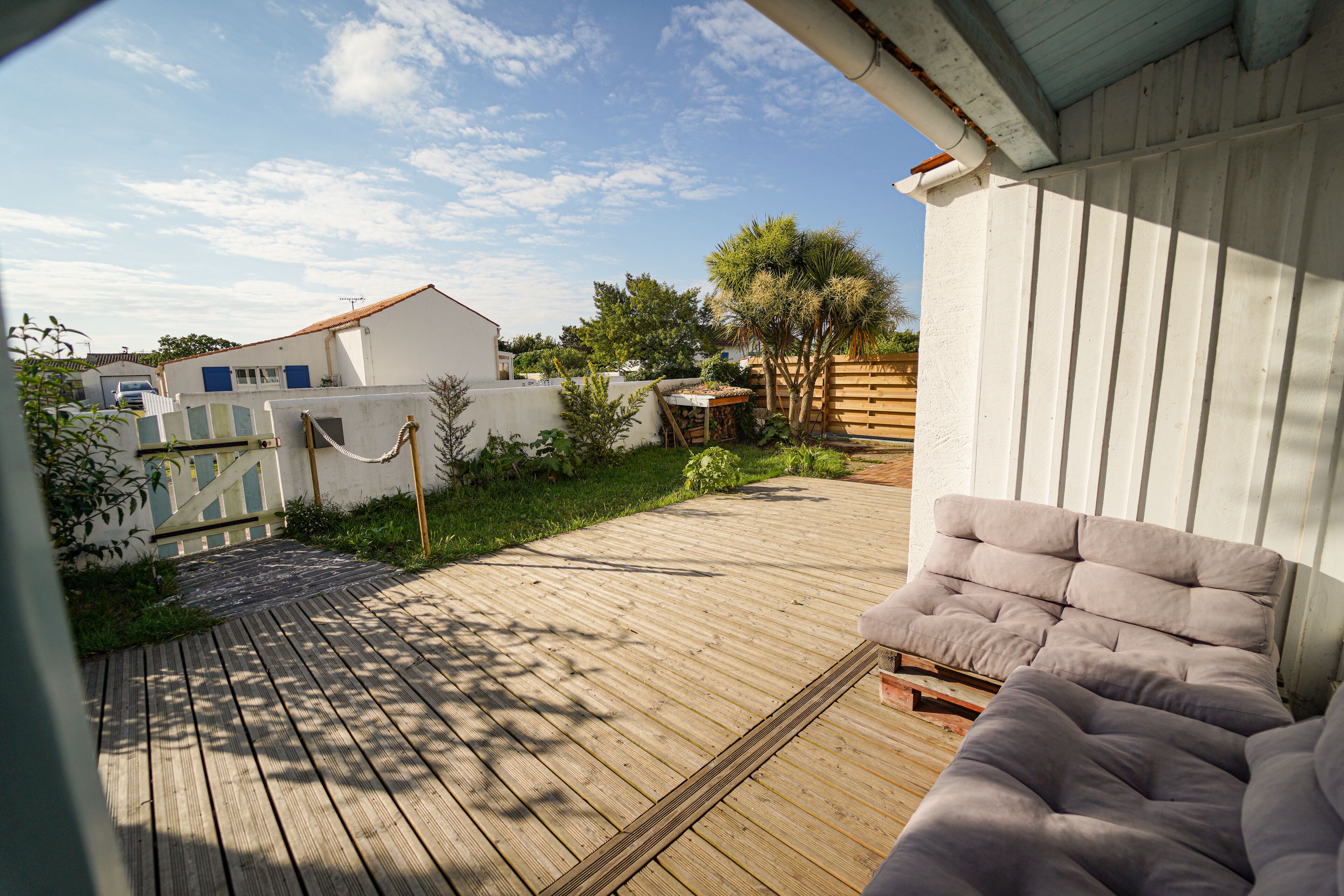 Une terrasse en bois avec un espace salon doté de coussins et un mur blanc.