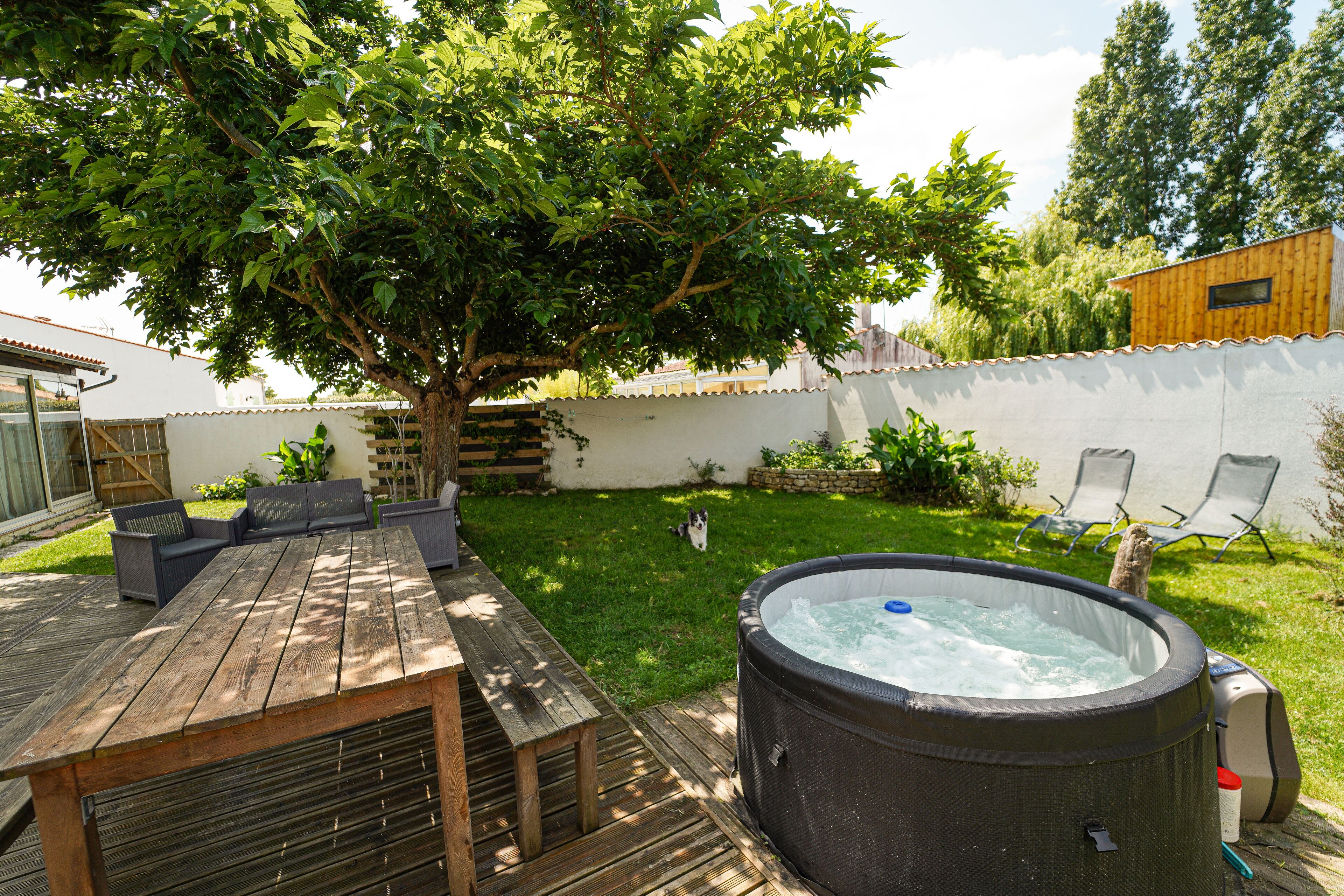 A backyard with a hot tub, wooden deck, and outdoor furniture.
