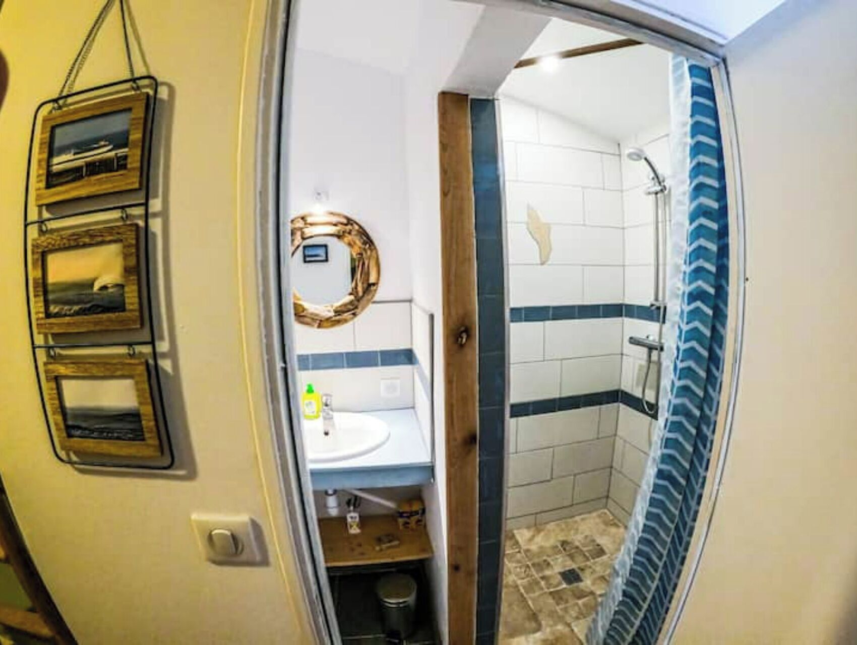 A bathroom with a shower, a sink, and a toilet. There are framed pictures on the wall.