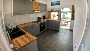 A modern kitchen with grey cabinets, a wooden countertop, and a view to the outside. - Oleron Surf House (Dolus-d'Oléron)