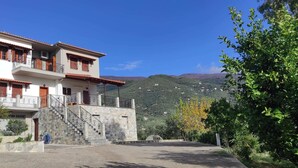 A two-story building with a stone staircase leading to a balcony, surrounded by greenery and hills in the background. - Gorgeous 3 bedrooms Apartment in Pilio (South Pelion)