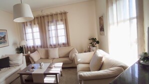 A living room with a beige sofa, a coffee table, and a lamp. There is a window with curtains and a painting on the wall. - Gorgeous 3 bedrooms Apartment in Pilio (South Pelion)