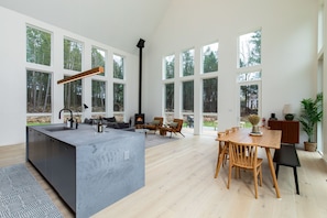 Amplia sala de estar con una isla grande, mesa de comedor de madera y múltiples ventanas con vistas al exterior.