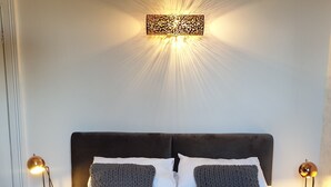 Un lit bien fait, avec deux oreillers, une tête de lit sombre et un luminaire fixé au mur au-dessus.