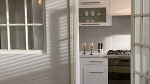 Une cuisine moderne avec des meubles blancs, une cuisinière à gaz et deux verres à vin posés sur le comptoir.