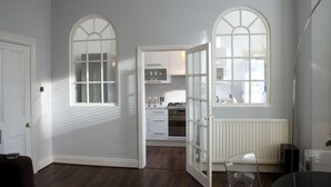 Une cuisine moderne avec des meubles blancs, un four encastré et une fenêtre donnant sur le salon.
