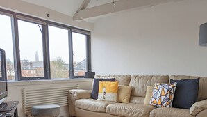 A modern living room with a leather sofa, a flat-screen TV, and a large window offering a city view. - Historic grade II listed Townhouse (Norwich)