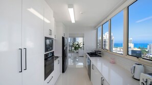 A modern kitchen with white cabinetry, a built-in oven, and a large window offering a view of the city and ocean.