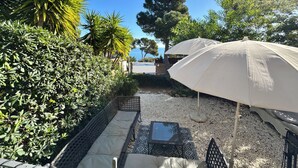 Une terrasse avec un parasol blanc, des sièges d’extérieur et une vue sur la mer.