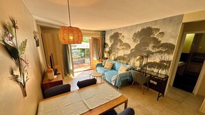 Un coin repas avec une table et des chaises en bois, un canapé avec des coussins à rayures et une fresque représentant des arbres sur le mur.