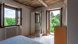 Un dormitorio con techo de madera, un radiador, una cama y vistas a zonas verdes a través de ventanas abiertas.