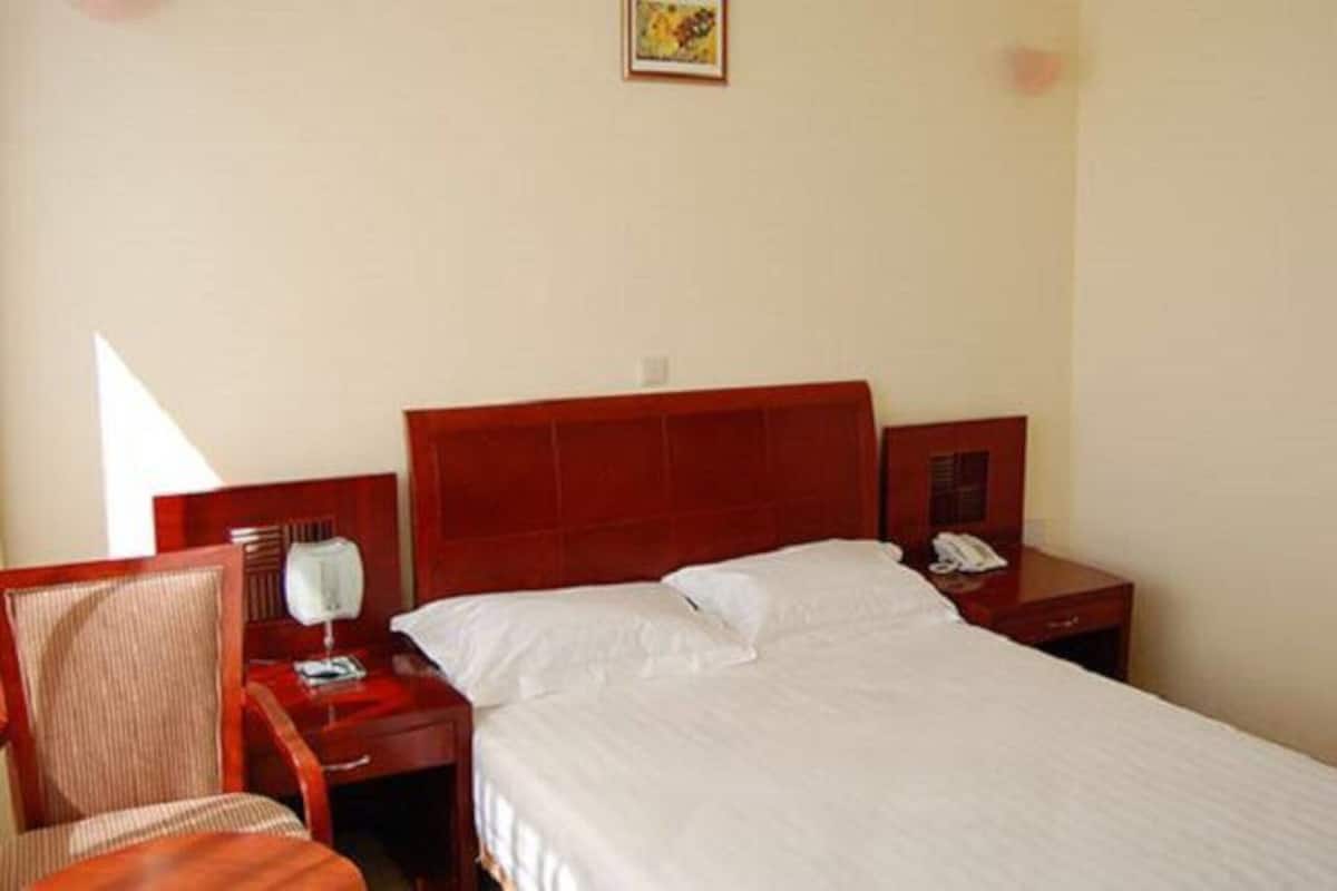 A hotel room with a large bed, a bedside table with a lamp, a chair, and a small table with a telephone.
