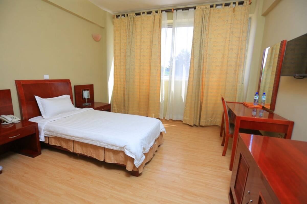 A hotel room with a bed, bedside table, desk, and a mirror.