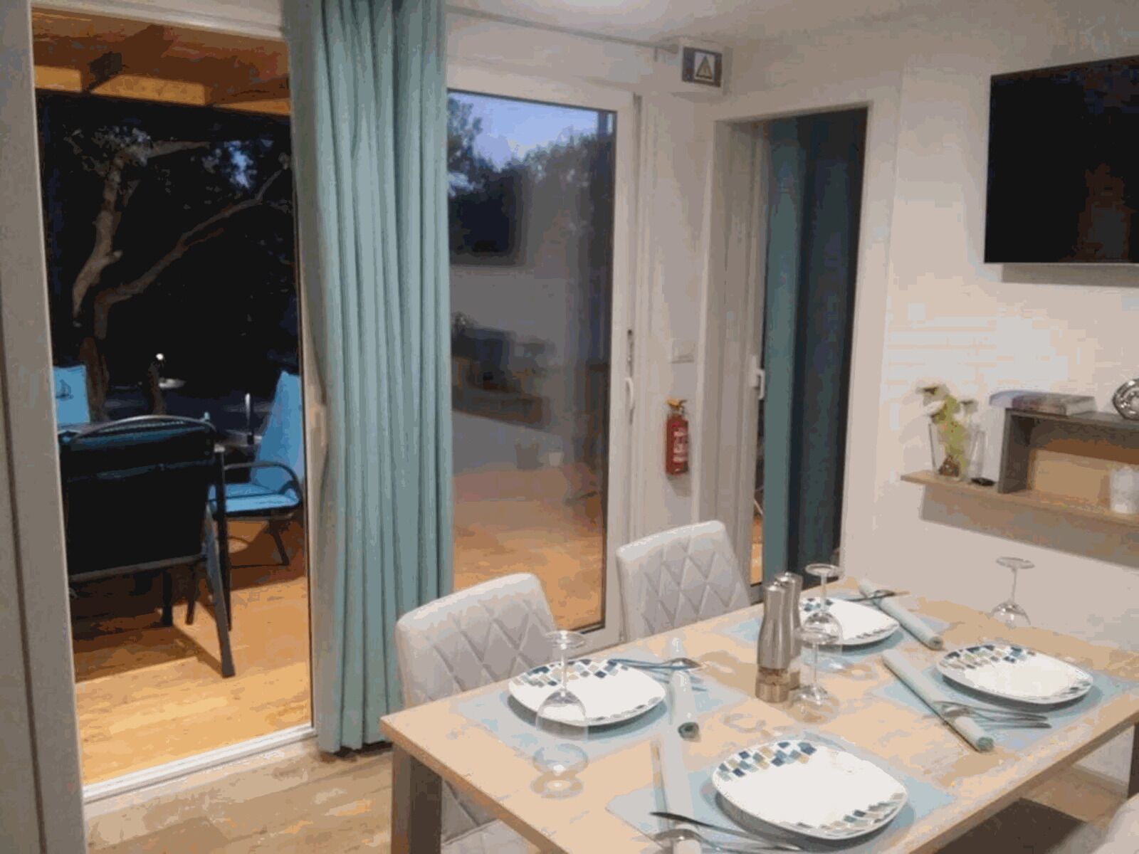 Un comedor con una mesa preparada para cuatro personas, una silla azul y vistas al exterior.