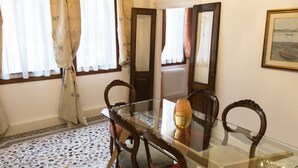 A dining area with a glass table, wooden chairs, a chandelier, and a tiled floor. - Ca' Nal Apartments, Corte Grimani Inn - BRAGOZZO (Venezia)