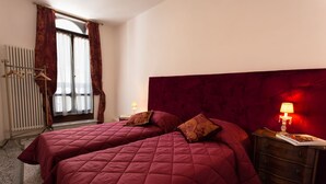 A hotel room with two beds, a red headboard, a wooden dresser, and a window with curtains. - Ca' Nal Apartments, Corte Grimani Inn - BRAGOZZO (Venezia)