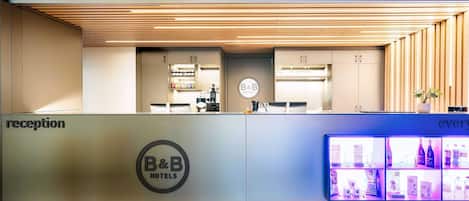 A reception area with a B&B Hotels sign, a reception desk, a coffee machine, and a display of amenities.