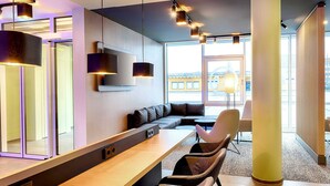 Eine moderne Hotellobby mit einer langen Rezeption, gemütlicher Sitzgelegenheiten, großen Fenstern und zeitgemäßen Beleuchtungselementen.