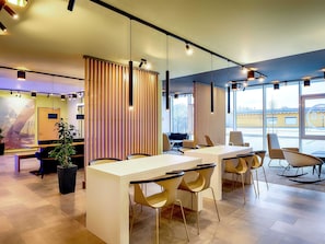 A modern office space with a white reception desk, several chairs, and a large window providing a view of the outside. - B&B Hotel Kehl (Kehl)