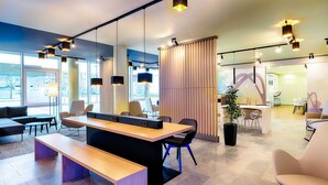 A modern office space with a long wooden table, several chairs, and a large window providing a view of the outside. - B&B Hotel Kehl (Kehl)