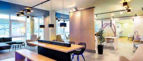 Un espace de bureau moderne avec une longue table en bois, plusieurs chaises et une grande fenêtre donnant sur l’extérieur.