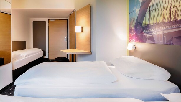 Ein Hotelzimmer mit einem großen Bett, einem kleinen Schreibtisch und einer Tür zu einem weiteren Raum.