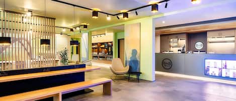 Un hall d’hôtel moderne comprenant un comptoir d’accueil, un espace salon et un bar.