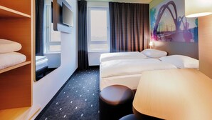 A hotel room with a bed, a desk, a chair, a mirror, a TV, and a painting of a bridge. - B&B Hotel Kehl (Kehl)