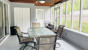 Un patio techado con mesa y sillas, ventanas amplias y un ventilador de techo.