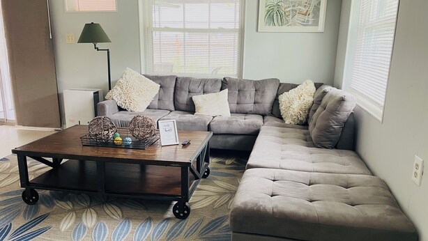 Una sala de estar con un sofá modular, una mesa de centro con objetos decorativos, una lámpara y un cuadro en la pared.