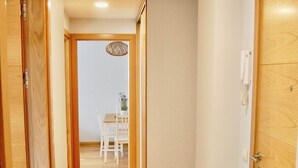 Ein Flur mit Holzboden, weißen Wänden und einem Essbereich im Hintergrund.