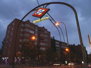 Un letrero de estación de Metro sobre un edificio con balcones, farolas y un cielo despejado.