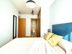 Un dormitorio con cama, mesita de noche, lámpara, luz de techo y puerta que da al baño.