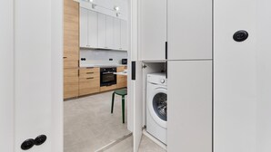 A modern kitchen with white cabinets, a green stool, and a washing machine. - Bright Apartment in Market Square | Pet Friendly and Place to Work (Wroclaw)