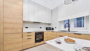 A modern kitchen with wooden cabinets, a built-in oven, a microwave, and a dining area with a white table and green chairs. - Bright Apartment in Market Square | Pet Friendly and Place to Work (Wroclaw)