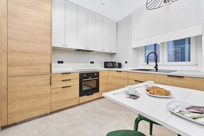 Cuina moderna amb armaris de fusta, forn encastrat, microones i zona de dinar amb taula blanca i cadires verdes.