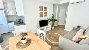 Een modern appartement met een eethoek, een grijze bank, een televisie en een keuken.