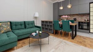 Una sala de estar moderna con un sofá verde, un comedor con sillas verdes y una cocina con armarios grises y salpicadero de ladrillo.