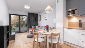 Una cocina moderna con microondas, un comedor con mesa para dos, y una sala de estar con sofá y televisor.