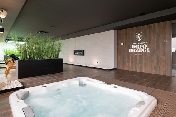 A modern indoor pool area with a hot tub, wooden flooring, and a wall-mounted TV.