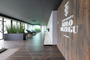 A modern lobby with a long bench area, a wall-mounted sign for 'APARTMENTY KOLO BRZEGU,' and a plant display.