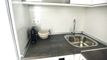 Cocina compacta con lavavajillas integrado, un lavamanos y una pequeña cesta de almacenamiento etiquetada con 'PAIN'.