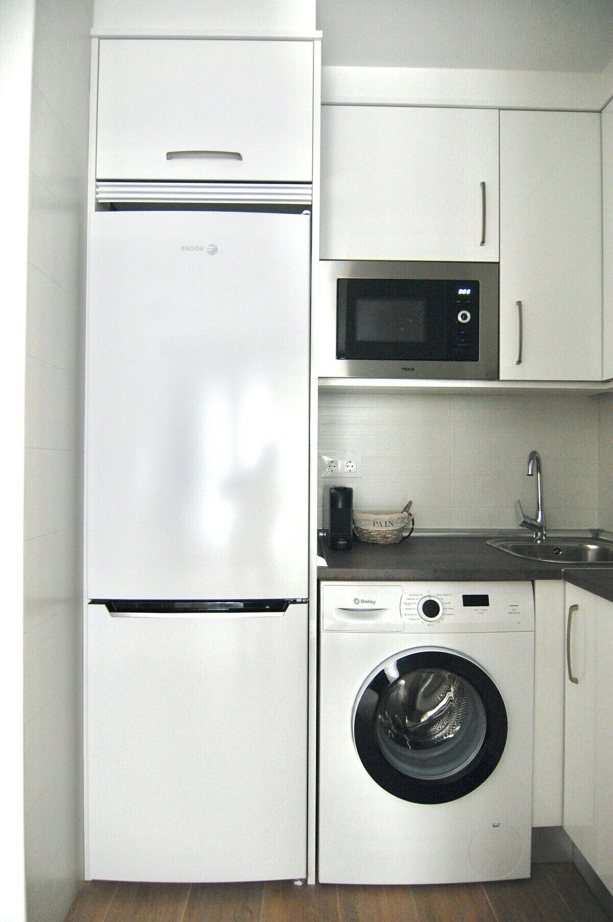Una cocina compacta con un refrigerador blanco, un microondas y una lavadora de carga frontal.