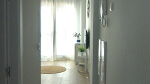 A hallway with a flat floor, a door on the left, and a window with curtains in the background. - Vivodomo | New, great location, optional parking (Madrid)