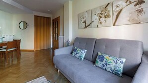 A living room with a grey sofa, two floral cushions, a dining table with chairs, and a wall-mounted mirror. - Vivodomo | Free parking, cozy, bright & central (Madrid)
