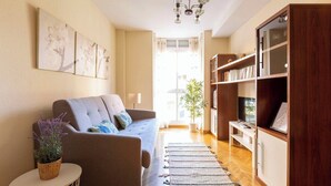 A living room with a sofa, a small side table with a plant, a bookshelf, and a large window. - Vivodomo | Free parking, cozy, bright & central (Madrid)