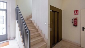 A staircase with a metal railing, a fire extinguisher on the wall, and a door with a fire exit sign. - Vivodomo | Free parking, cozy, bright & central (Madrid)